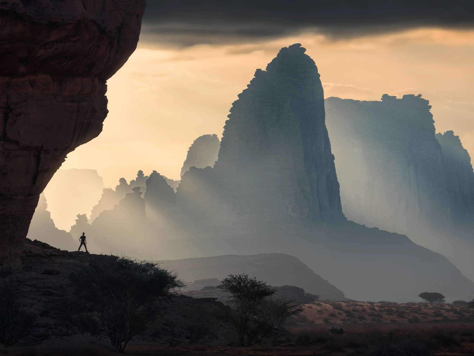 Silhouette of a man standing on a rocky cliff with dramatic sun rays and towering sandstone formations in the desert of Saudi Arabia