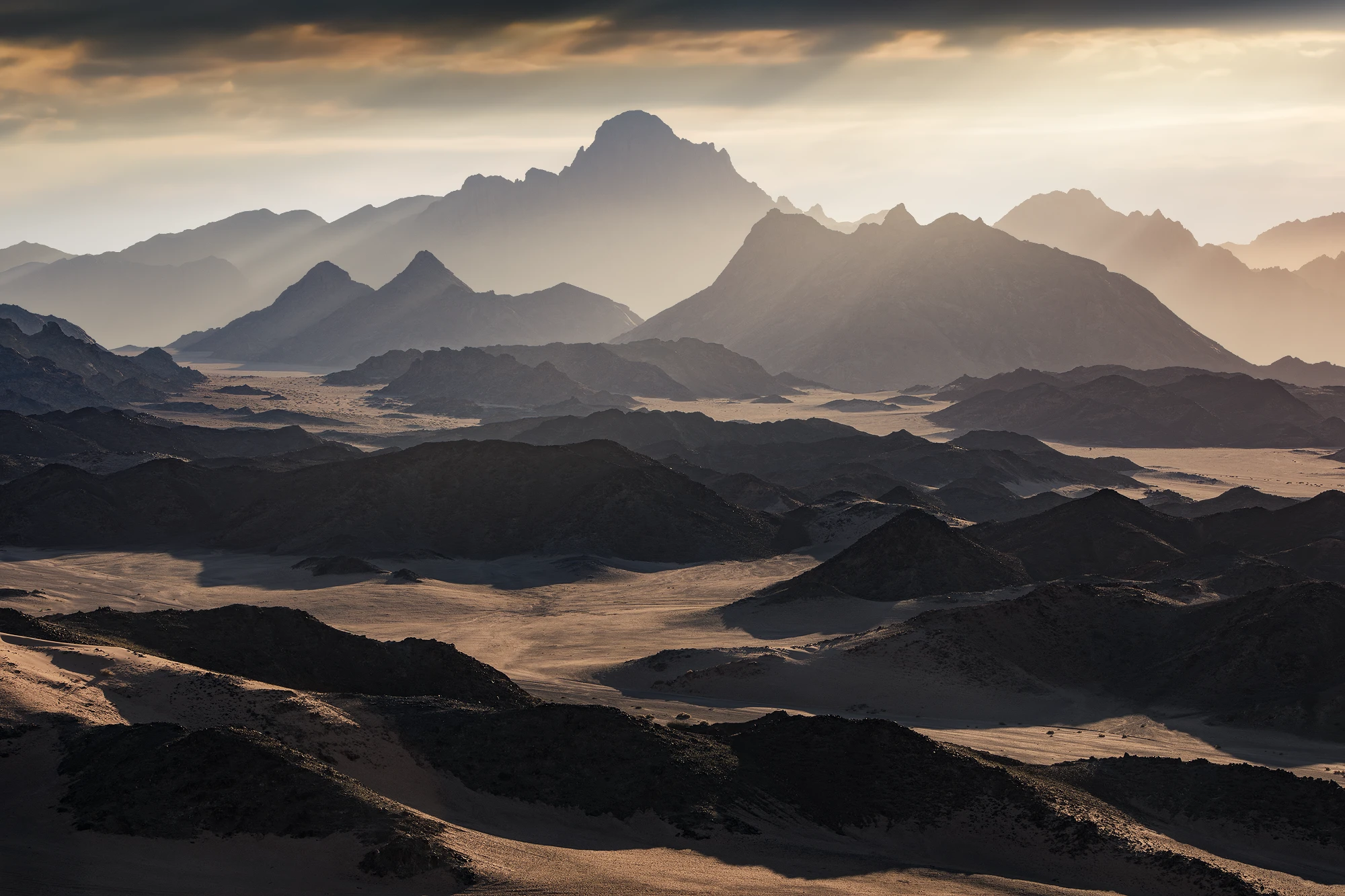 Layered desert mountains and dunes at sunrise in Tabuk near NEOM, Saudi Arabia with soft haze and dramatic light