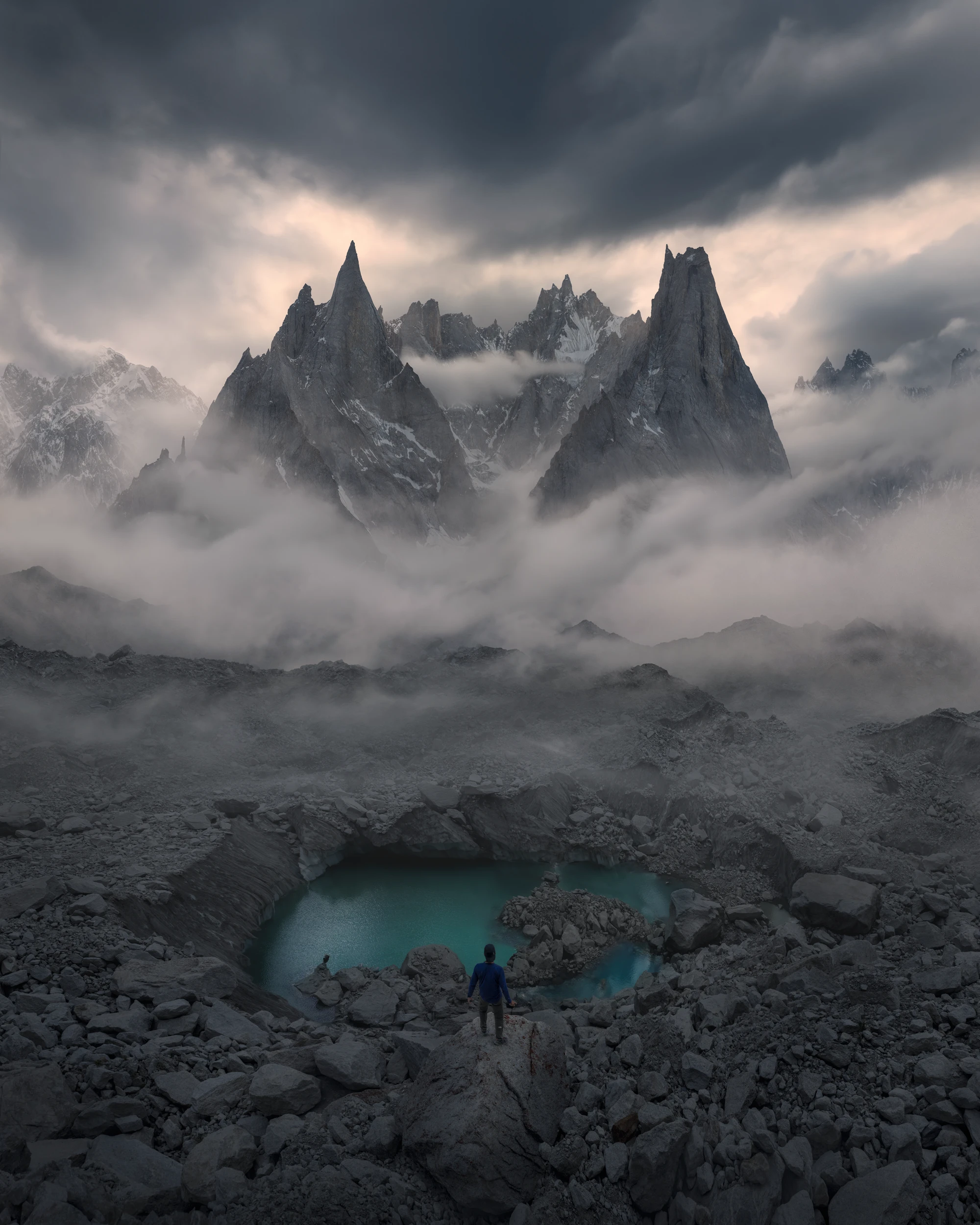 A person stands above a turquoise mountain lake beneath mist-shrouded rocky peaks in Pakistan’s Karakoram mountains.